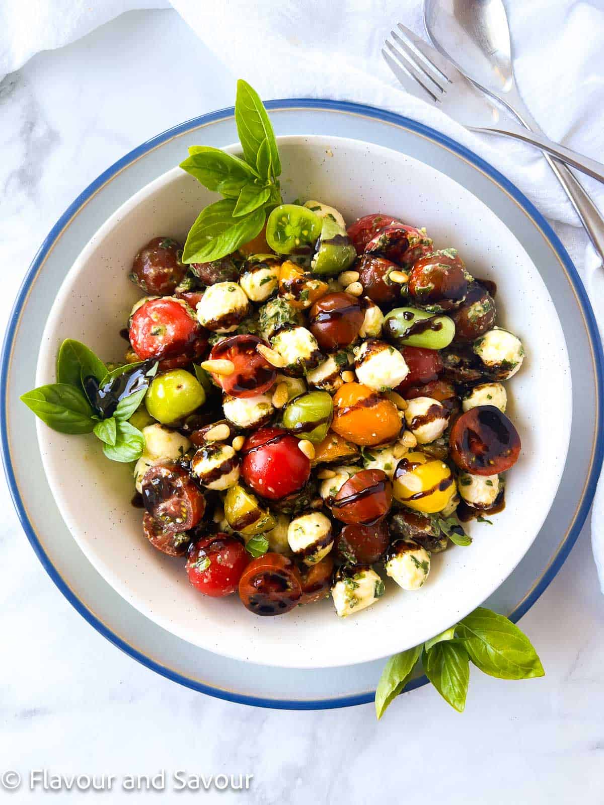 Easy Pesto Caprese Salad with Cherry Tomatoes drizzled with balsamic glaze and garnished with fresh basil leaves and pine nuts.