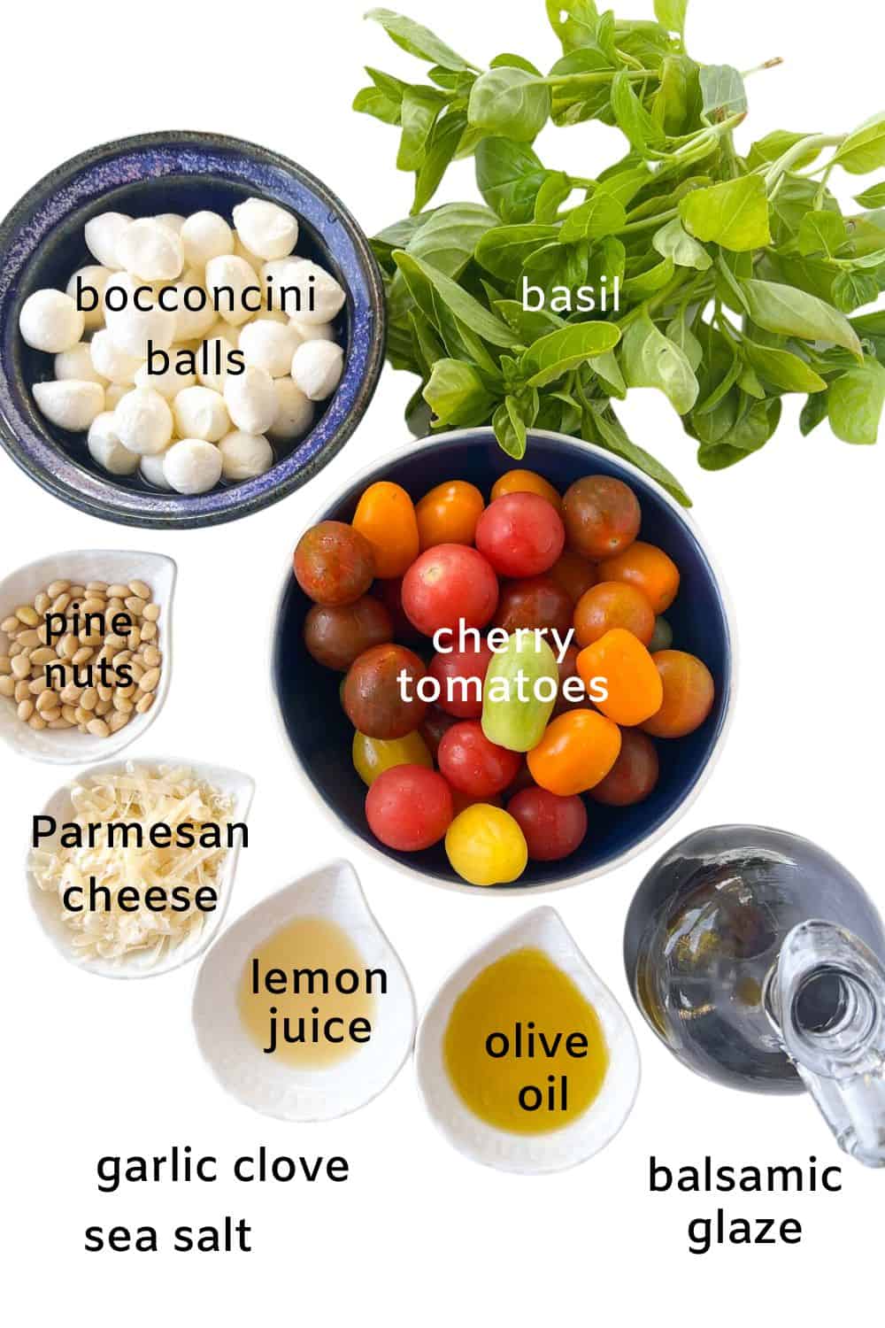 Ingredients for Pesto Caprese Salad: basil, tomatoes, bocconcini balls, pine nuts, Parmesan cheese, garlic, lemon juice, olive oil, balsamic glaze, sea salt.