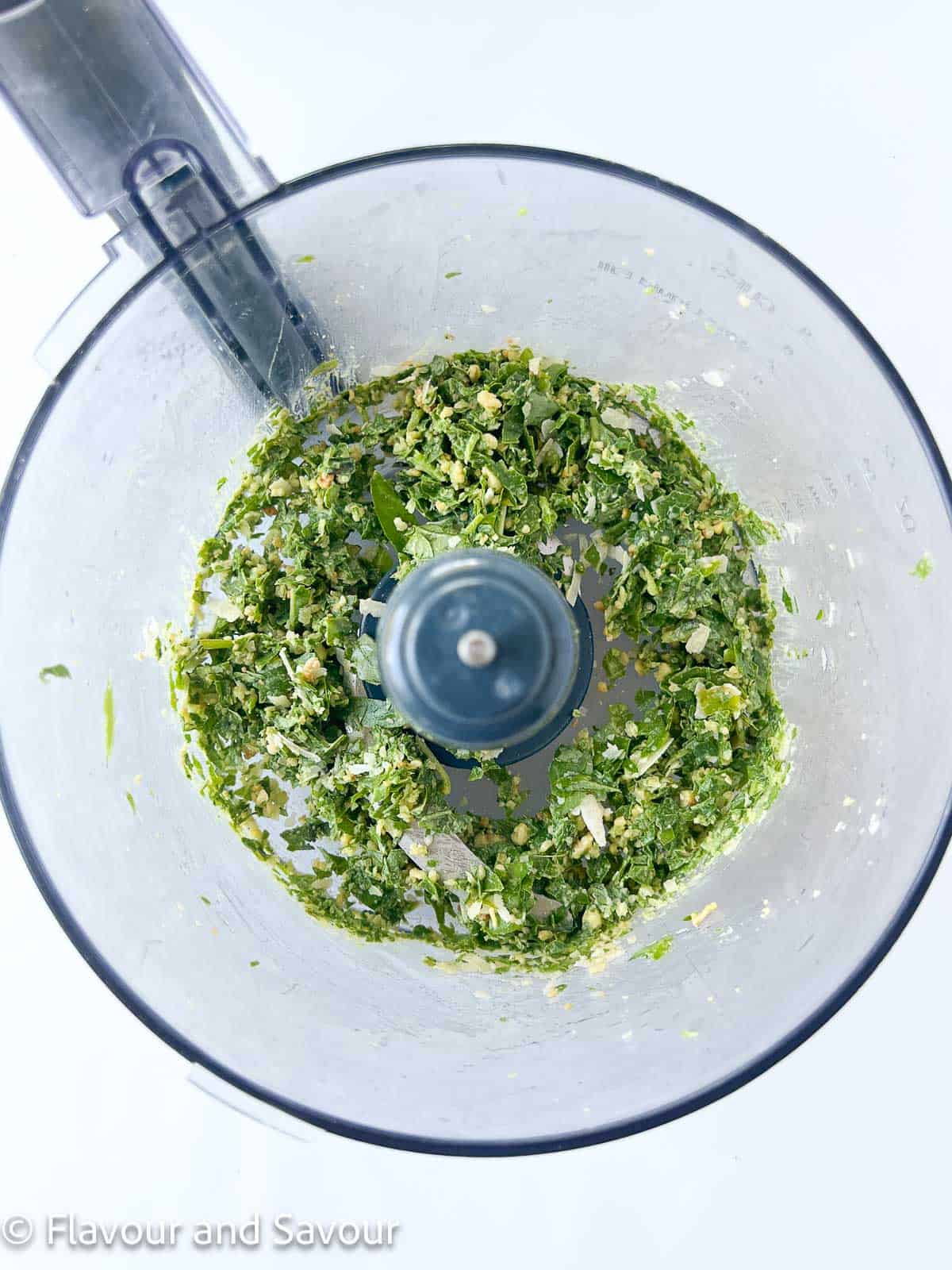 Finely chopped pesto ingredients in a food processor bowl.