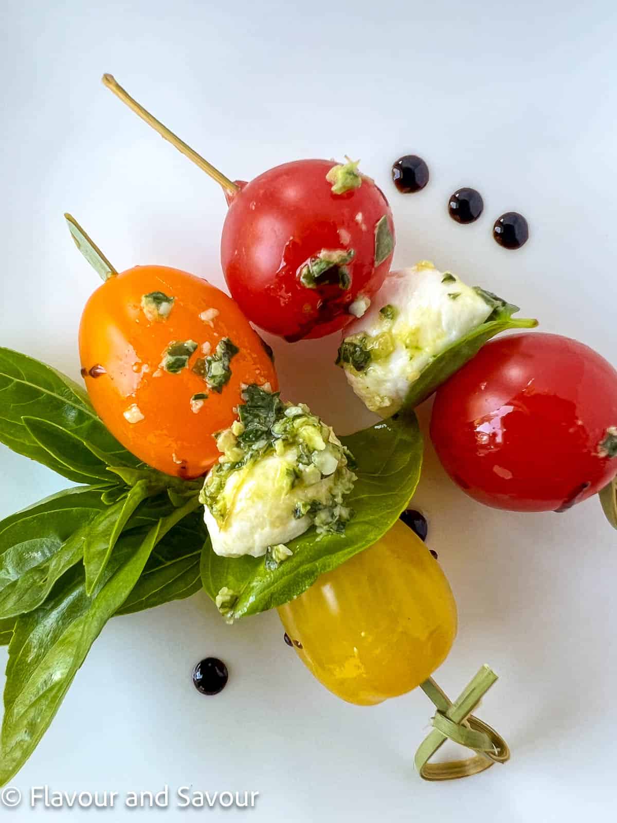 Pesto Caprese Skewers made with cherry tomatoes, bocconcini balls, pesto and a basil lear.