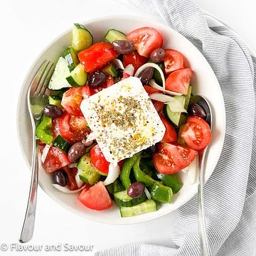Overhead view of a bowl of Greek salad with a slab of feta cheese.