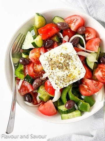 Overhead view of a bowl of Greek salad with a slab of feta cheese.