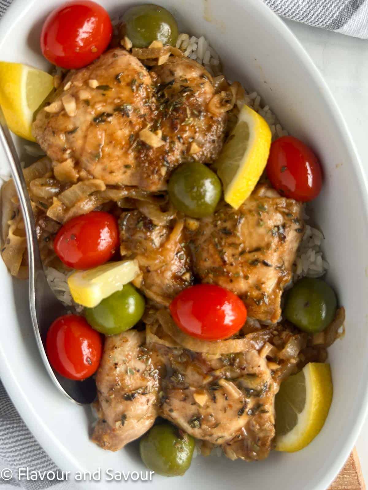 A bowl of Moroccan lemon chicken thighs with olives, tomatoes and fresh lemon slices.
