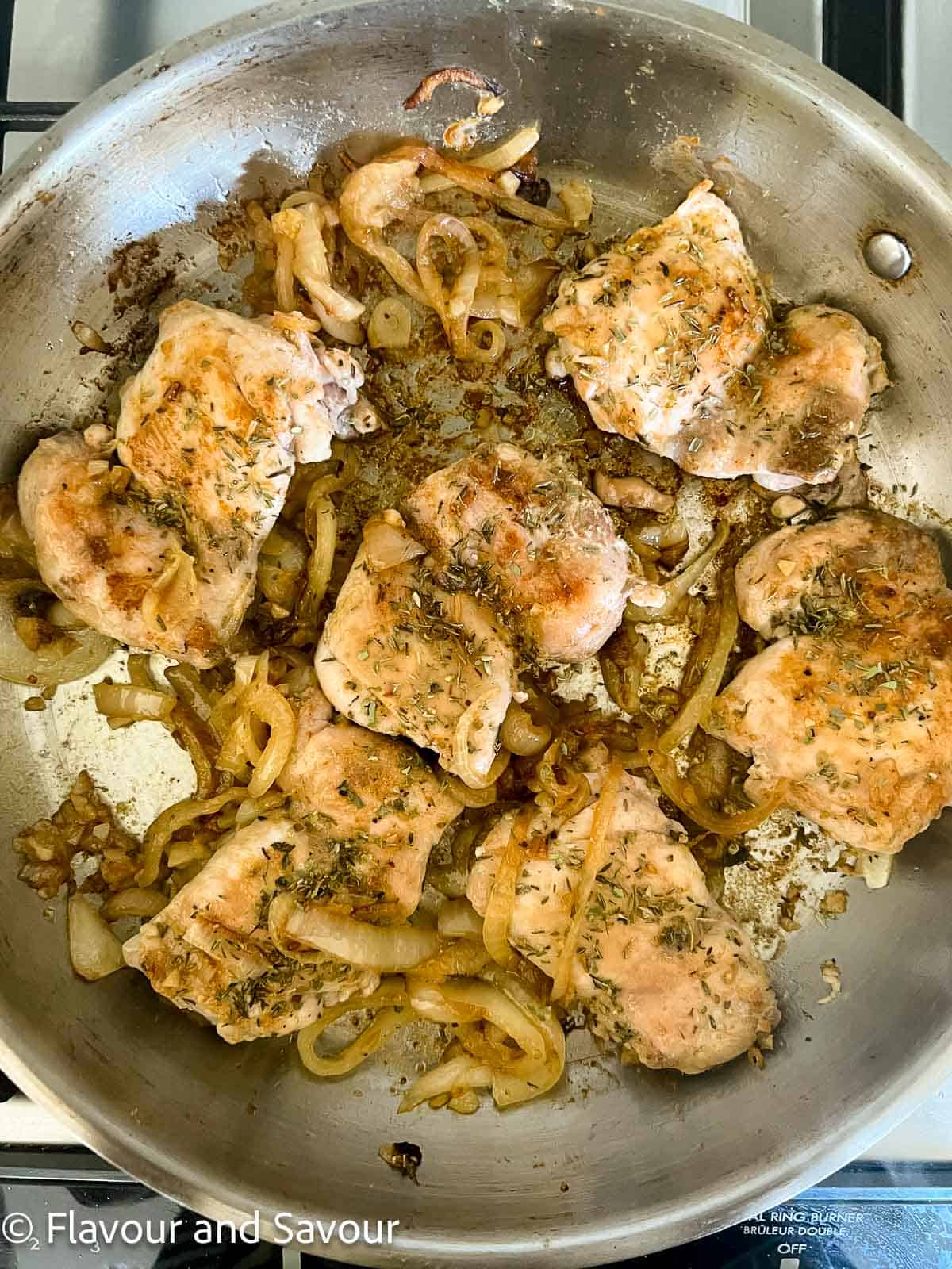 Seared chicken thighs with onions and garlic in a skillet.