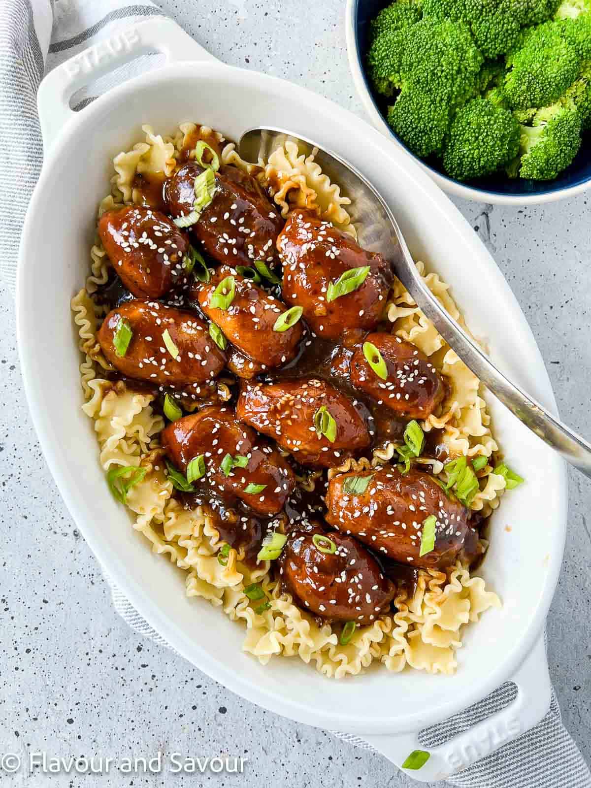 Overhead view of an oval serving dish with slow cooker sticky chicken thighs on a bed of noodles.