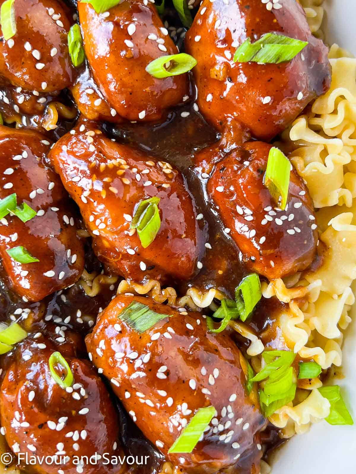 Closeup view of chicken thighs with sticky chicken sauce garnished with sesame seeds and green onions.