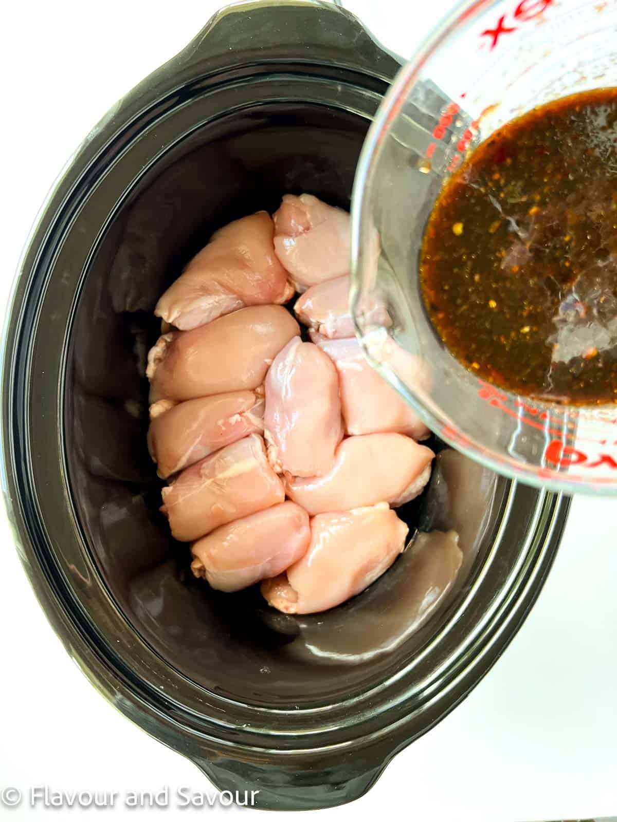 Pouring sauce over raw chicken thighs in a slow cooker.
