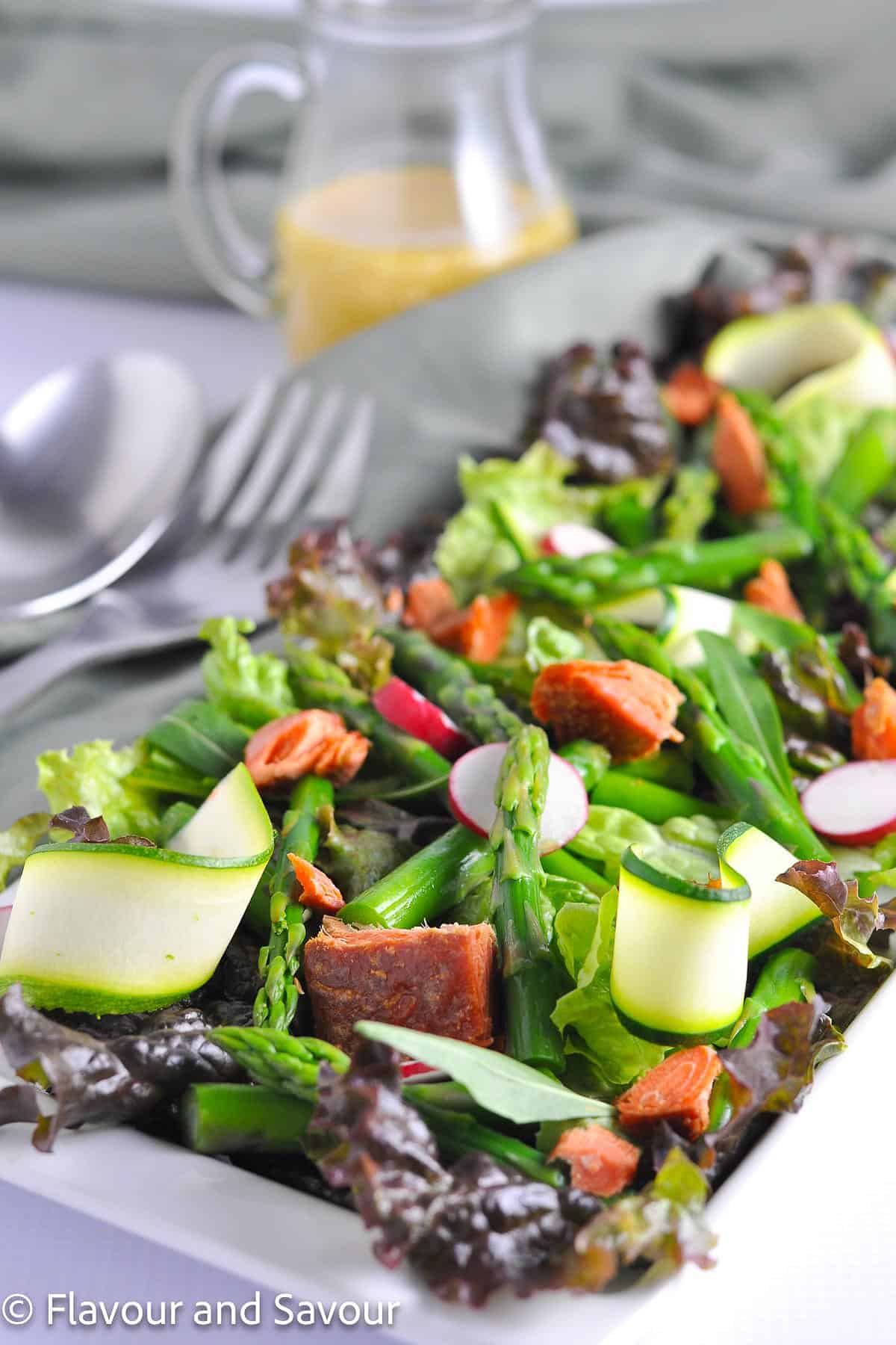 A platter of smoked salmon asparagus salad with a jug of sesame miso vinaigrette in the background.