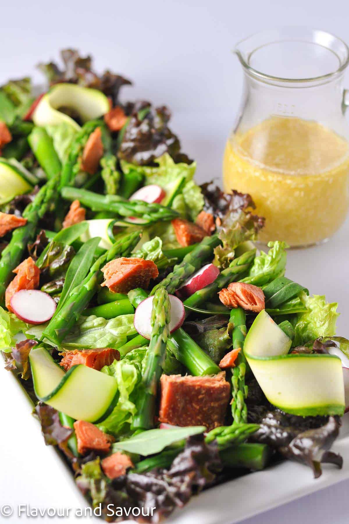 A rectangular platter with smoked salmon salad with asparagus, zucchini ribbons, radishes on a bed of fresh greens.