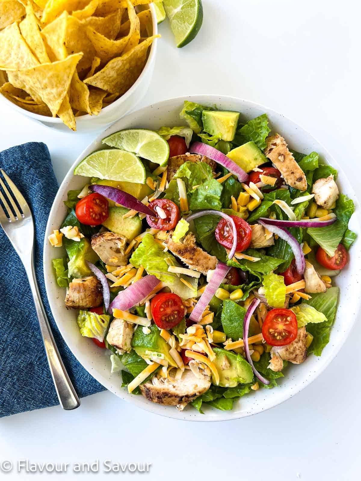 Overhead view of a bowl of chicken taco salad with a small bowl of tortilla chips beside it.