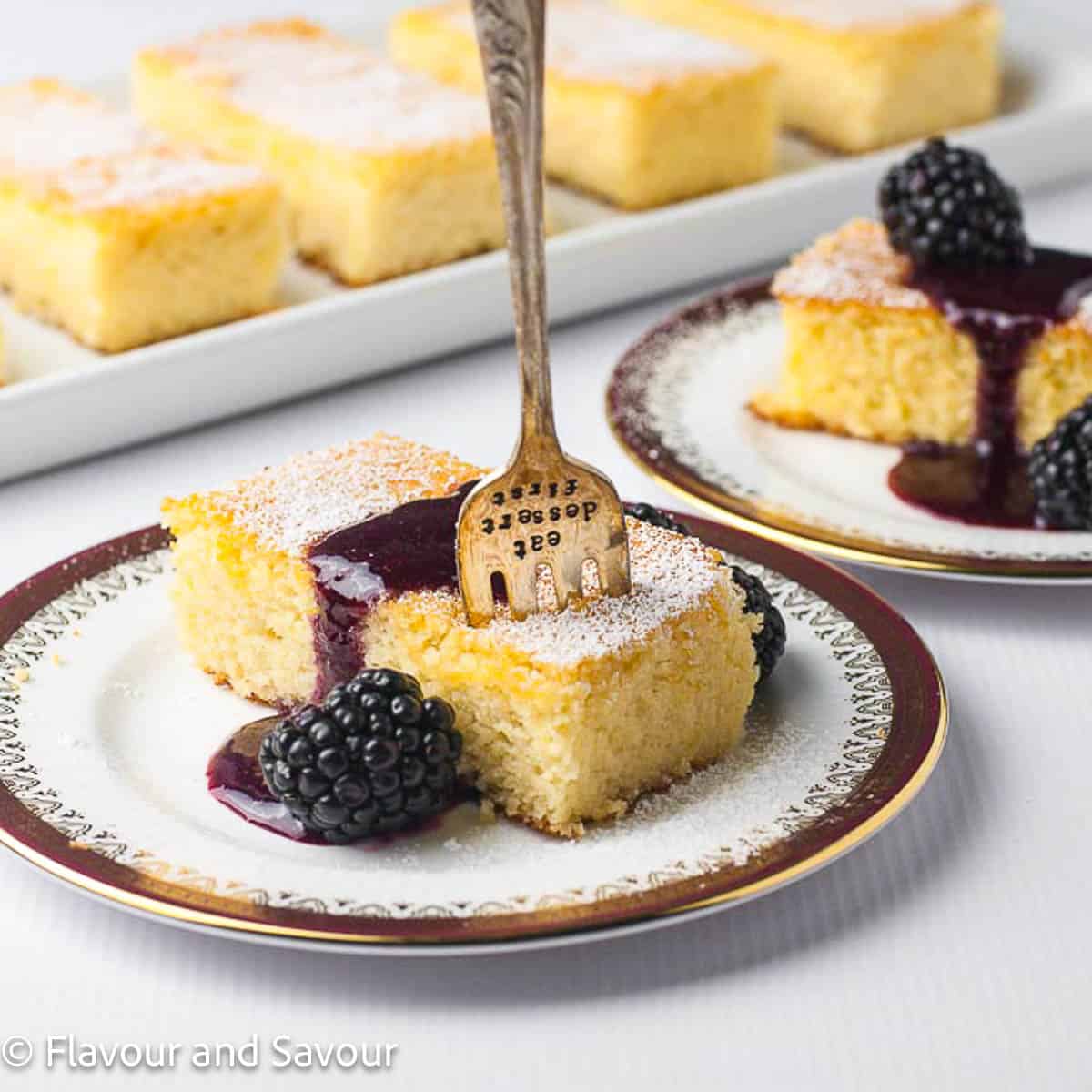 A slice of flourless lemon ricotta cake topped with blackberry sauce with a fork standing upright in it.