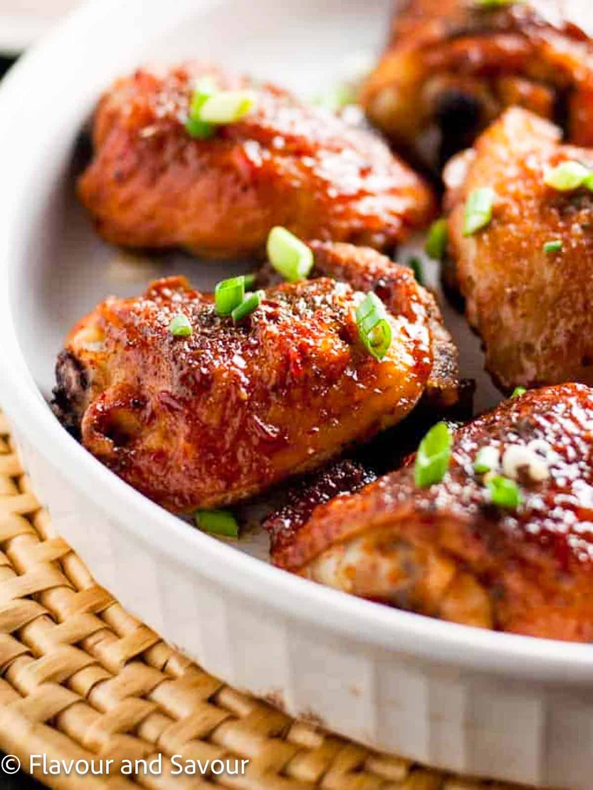 Smoky chipotle honey-mustard glazed chicken thighs in a round white serving dish garnished with sliced green onions.