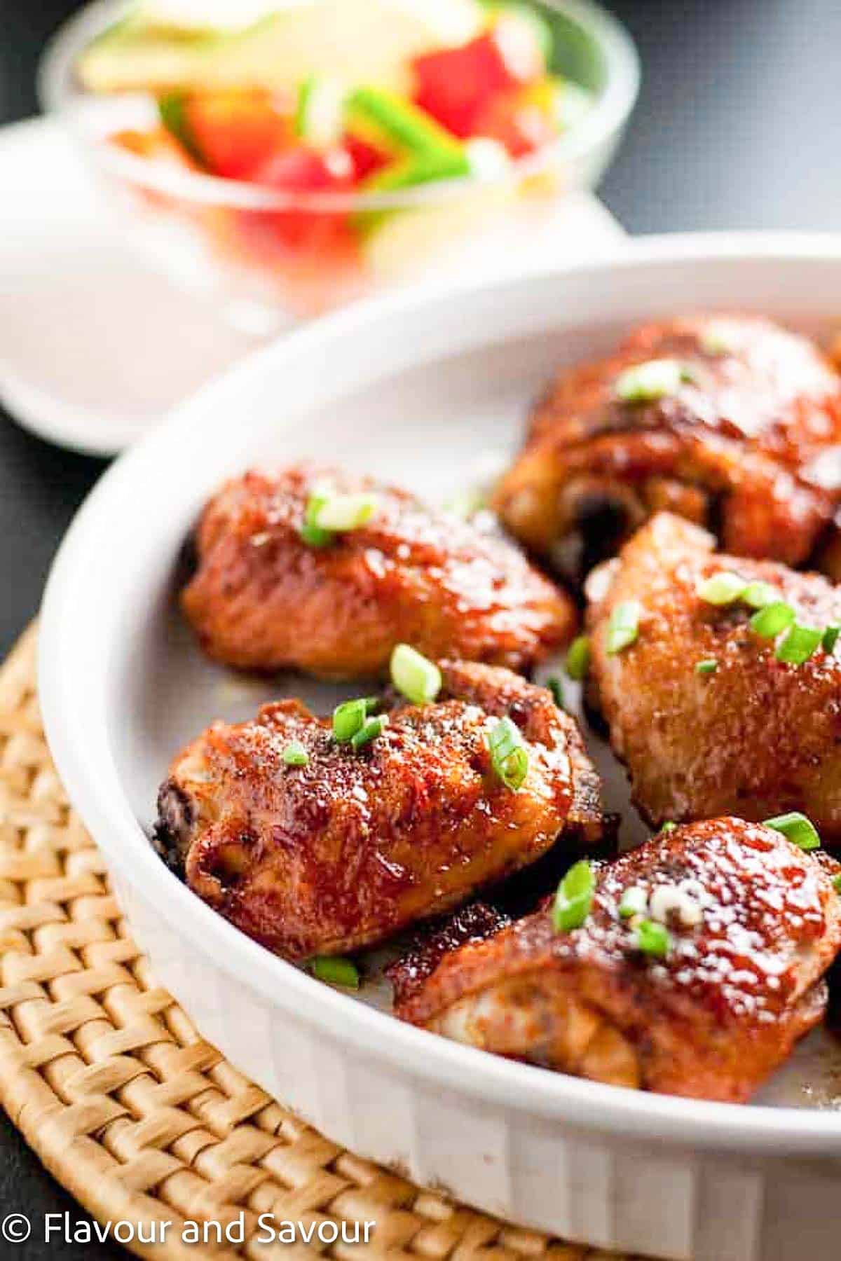 A serving dish with chipotle honey-mustard glazed chicken thighs with a small salad in the background.