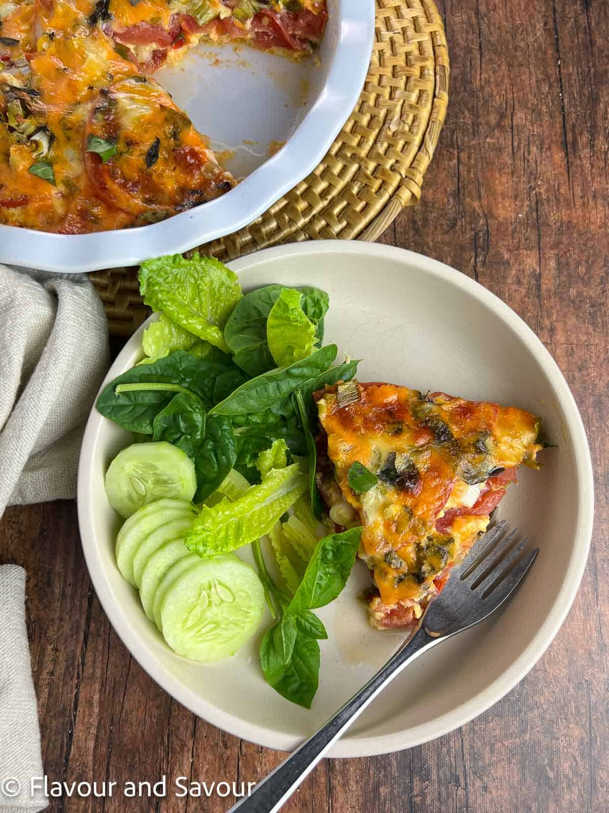 A wedge of tomato cheese pie with a green salad beside it.