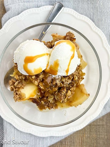 Overhead view of a bowl of apple pecan crisp with ice cream and caramel sauce.