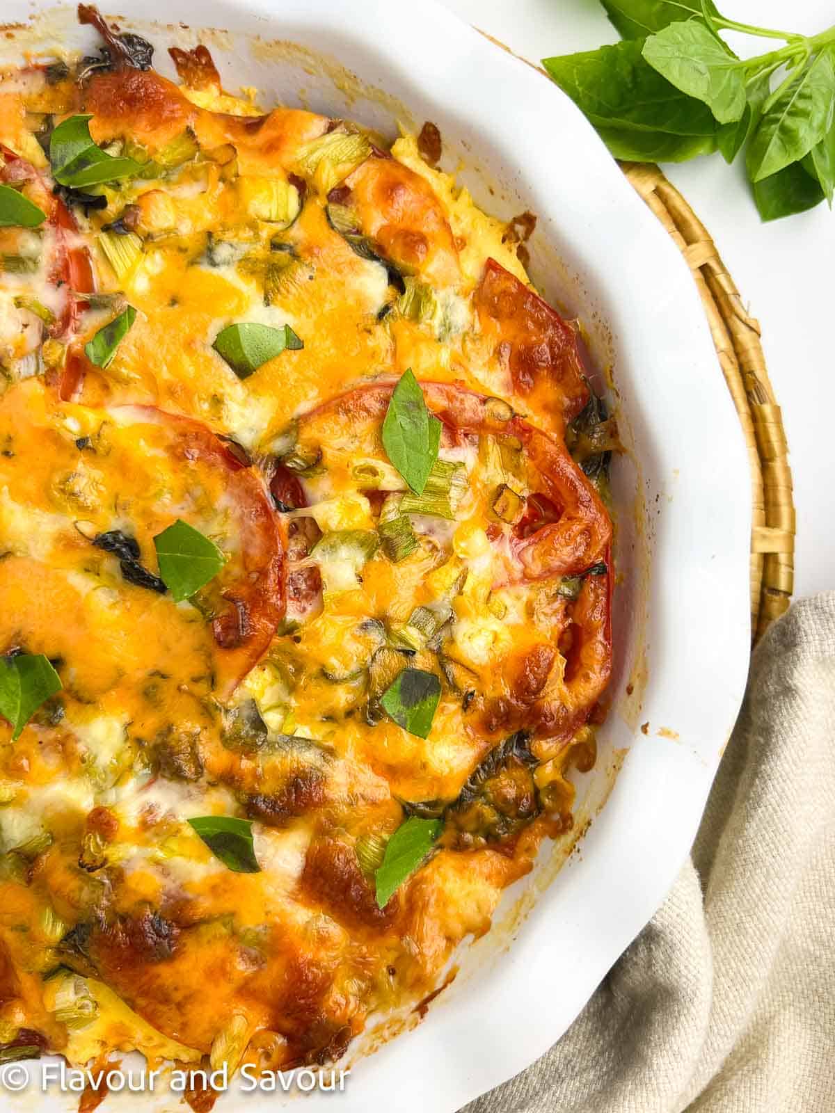 Closeup view of the side of crustless tomato pie in a ceramic pie dish.