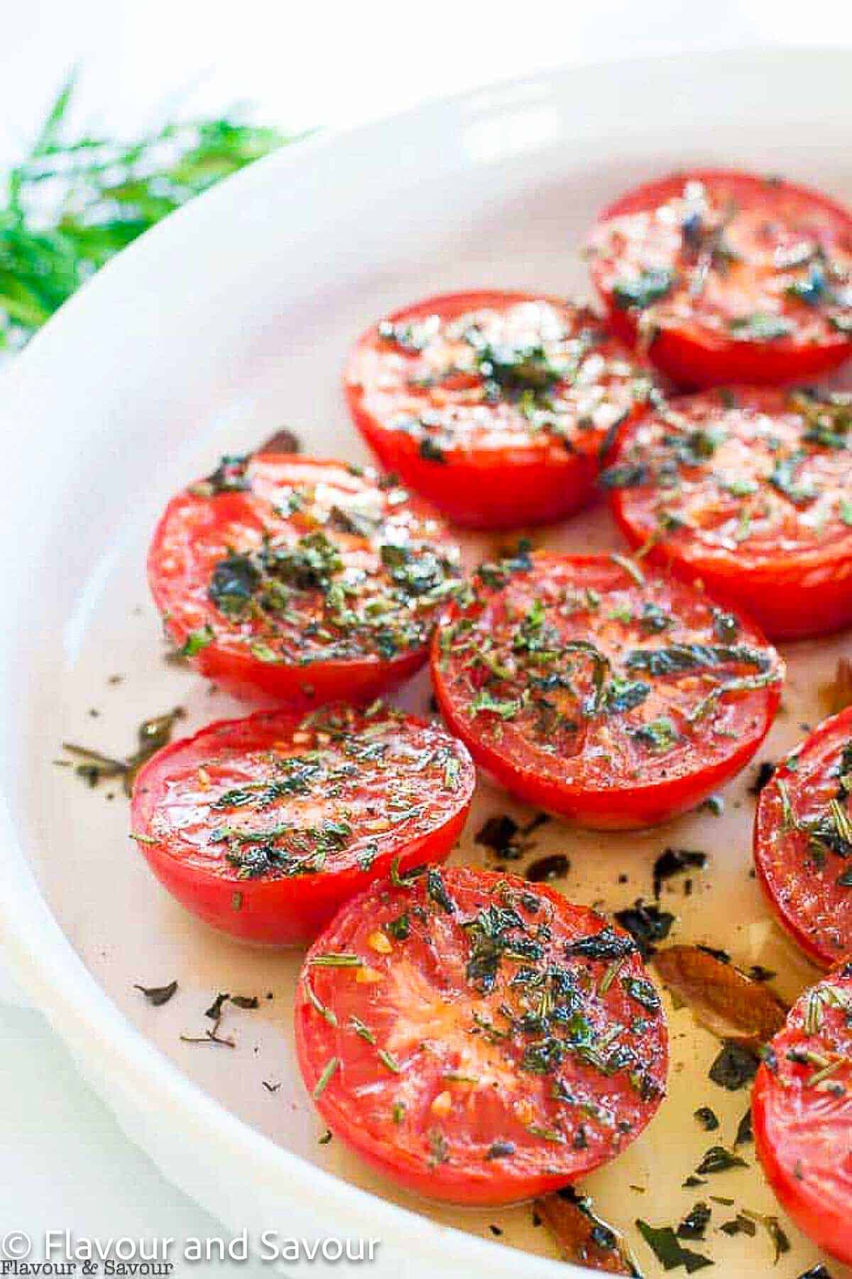A white serving dish with broiled Italian tomatoes with herbs and garlic-infused olive oil.