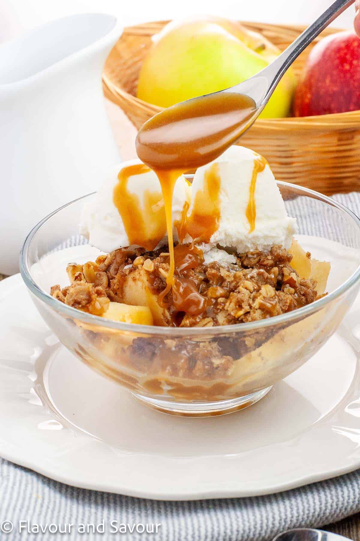 Spooning caramel sauce on apple crisp with a pecan oat crumble topping.