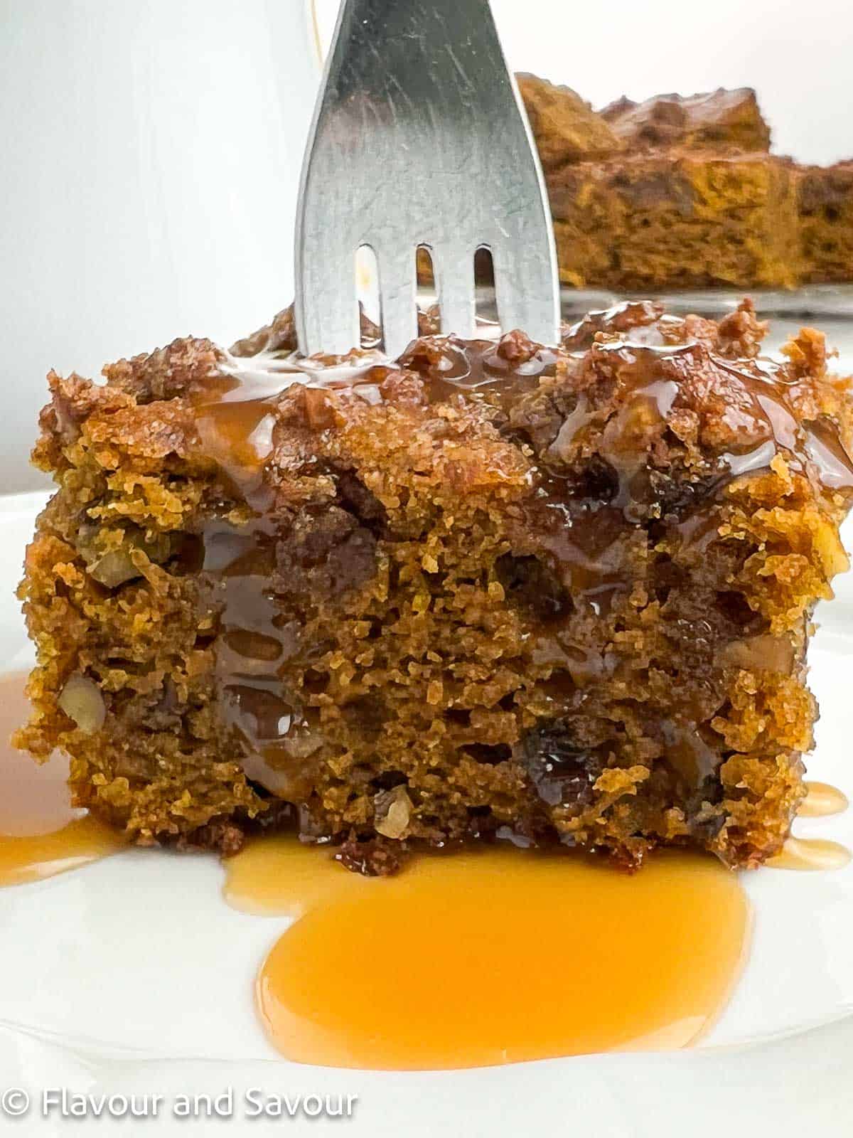 Extreme closeup view of a piece of pumpkin pecan coffee cake with caramel sauce and a fork.