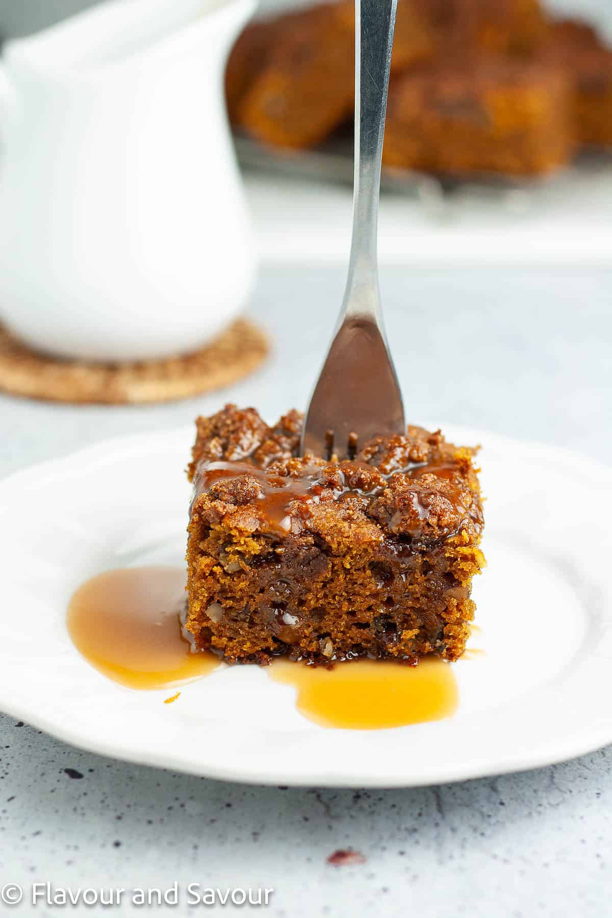 A slice of pumpkin coffee cake drizzled with caramel sauce with a fork standing straight up in it.