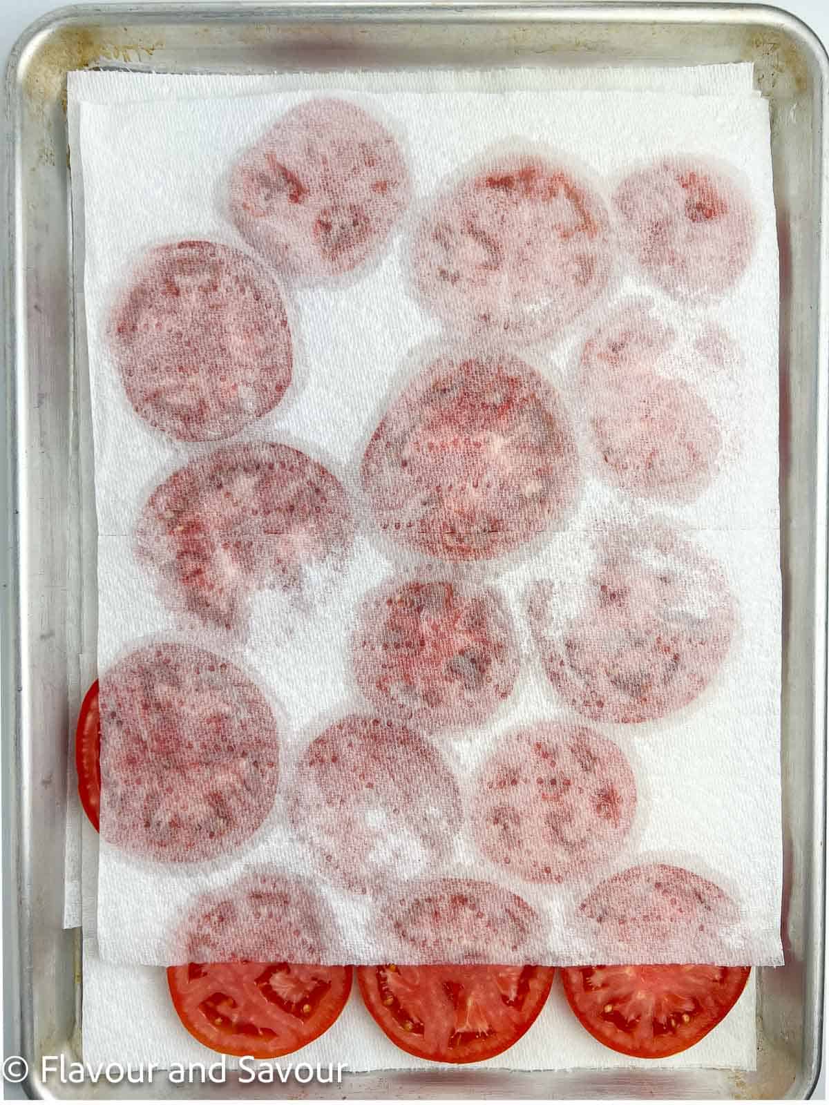 Paper towel on top of a baking sheet of sliced tomatoes.