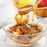 A spoonful of homemade caramel sauce over a bowl of apple pecan crisp.