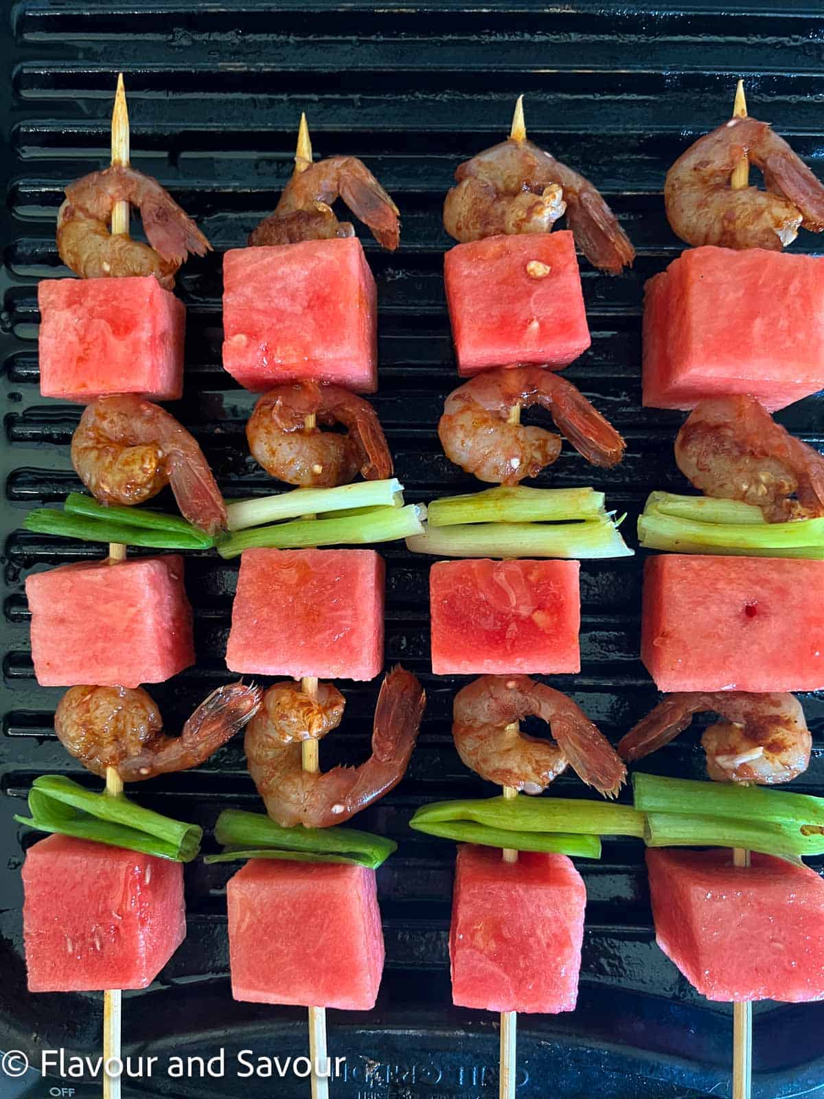 Skewers of watermelon, green onions and spot prawns on an indoor grill.