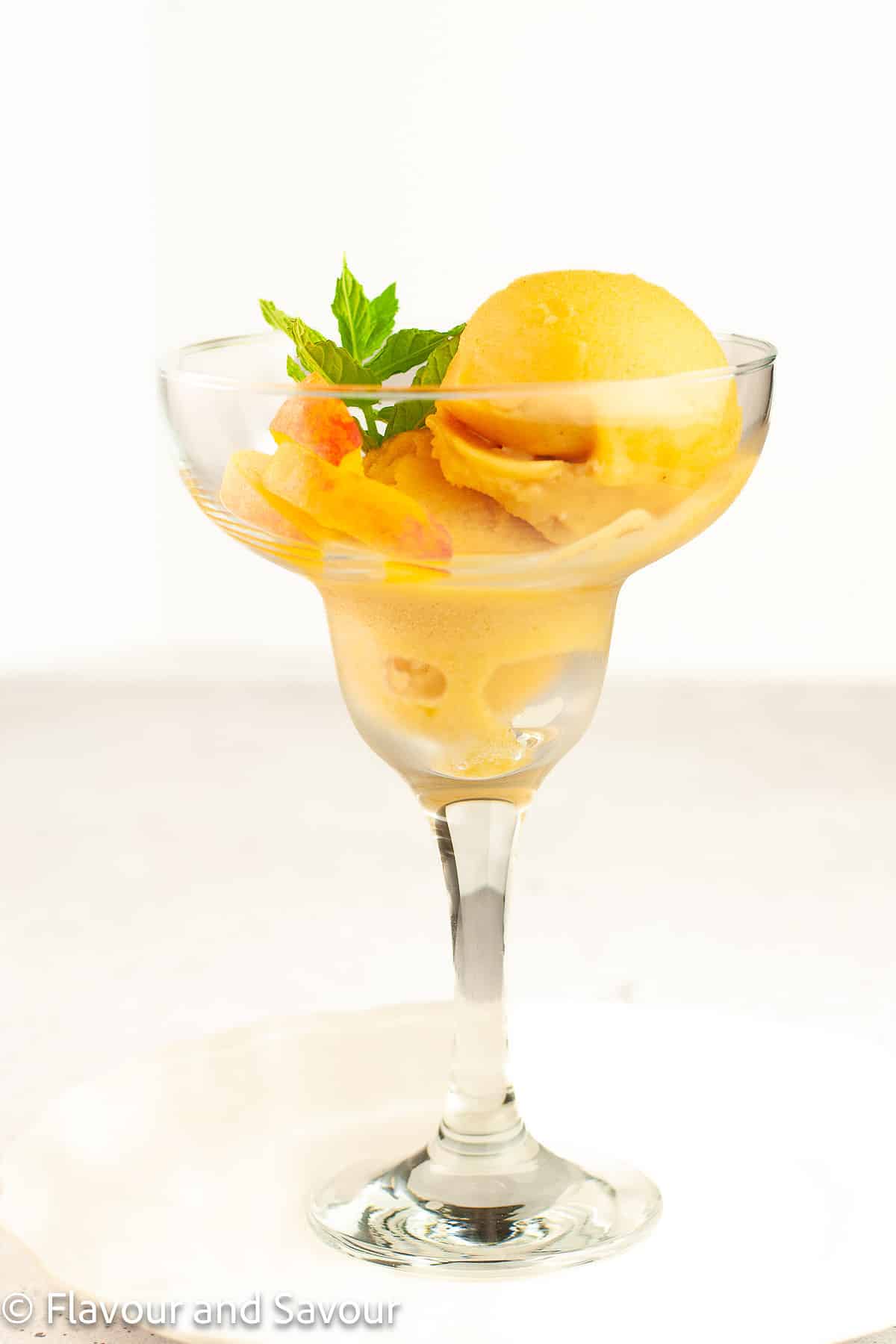 Peach ginger sorbet in a stemmed dessert glass with a sprig of mint.