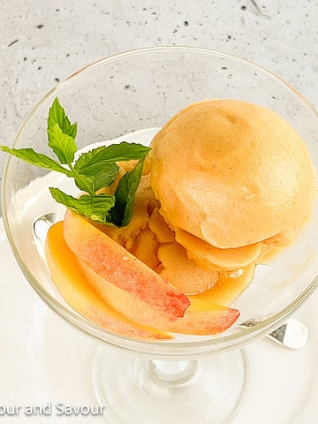 Peach sorbet in a dessert glass with fresh peach slices.