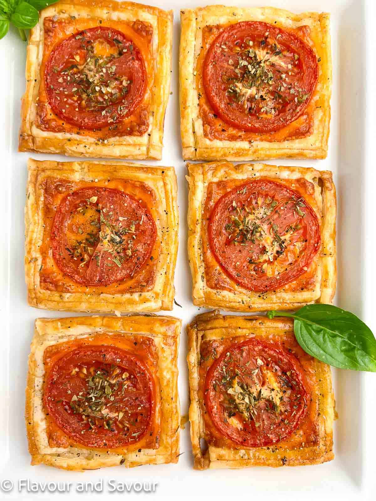 Overhead view of 6 puff pastry tomato tarts on a white serving plate.