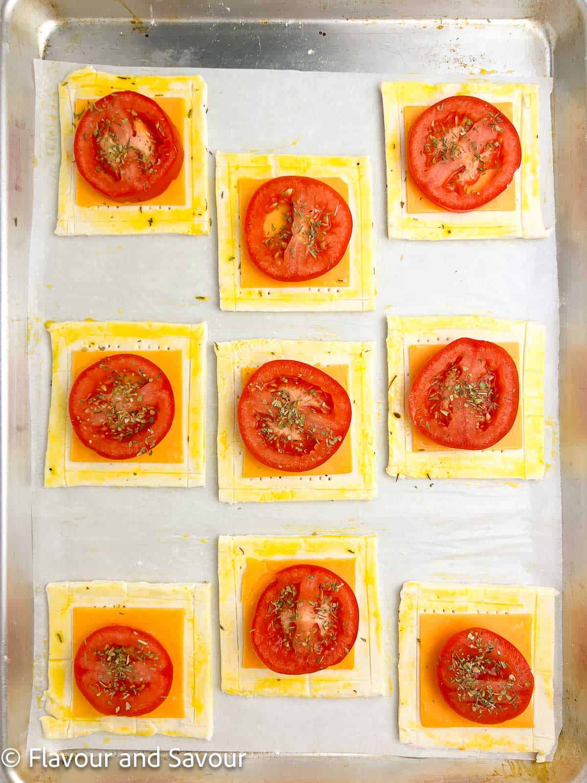 Assembling puff pastry cheddar tomato tarts on a baking sheet.