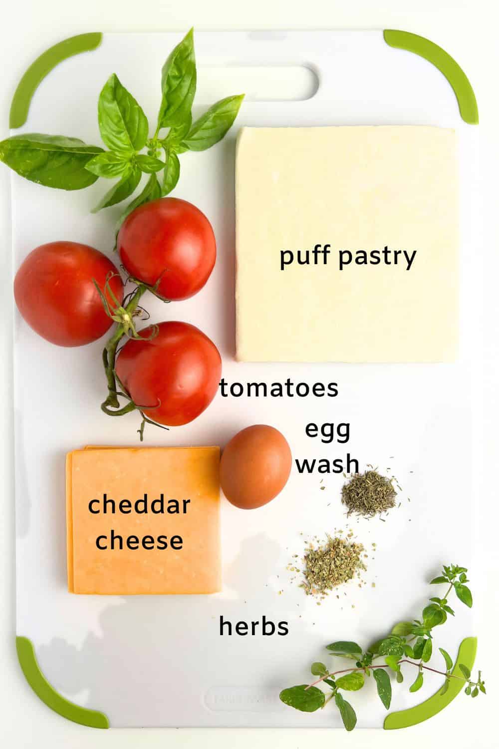 Ingredients for puff pastry cheese and tomato tarts: cheddar cheese, puff pastry, tomatoes, herbs, egg for an egg wash.