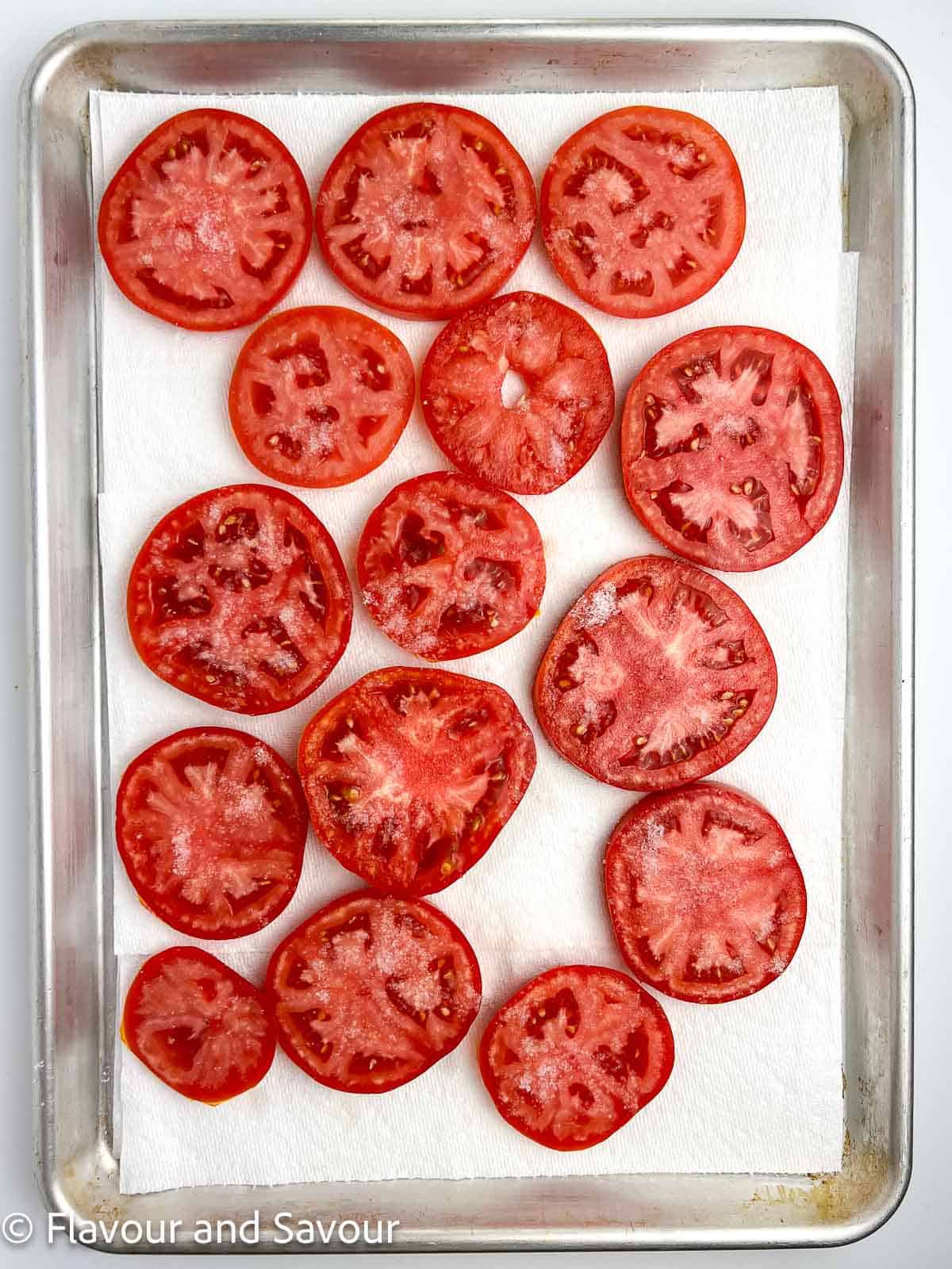 Tomato slices on a sheet of paper towel on a baking sheet.
