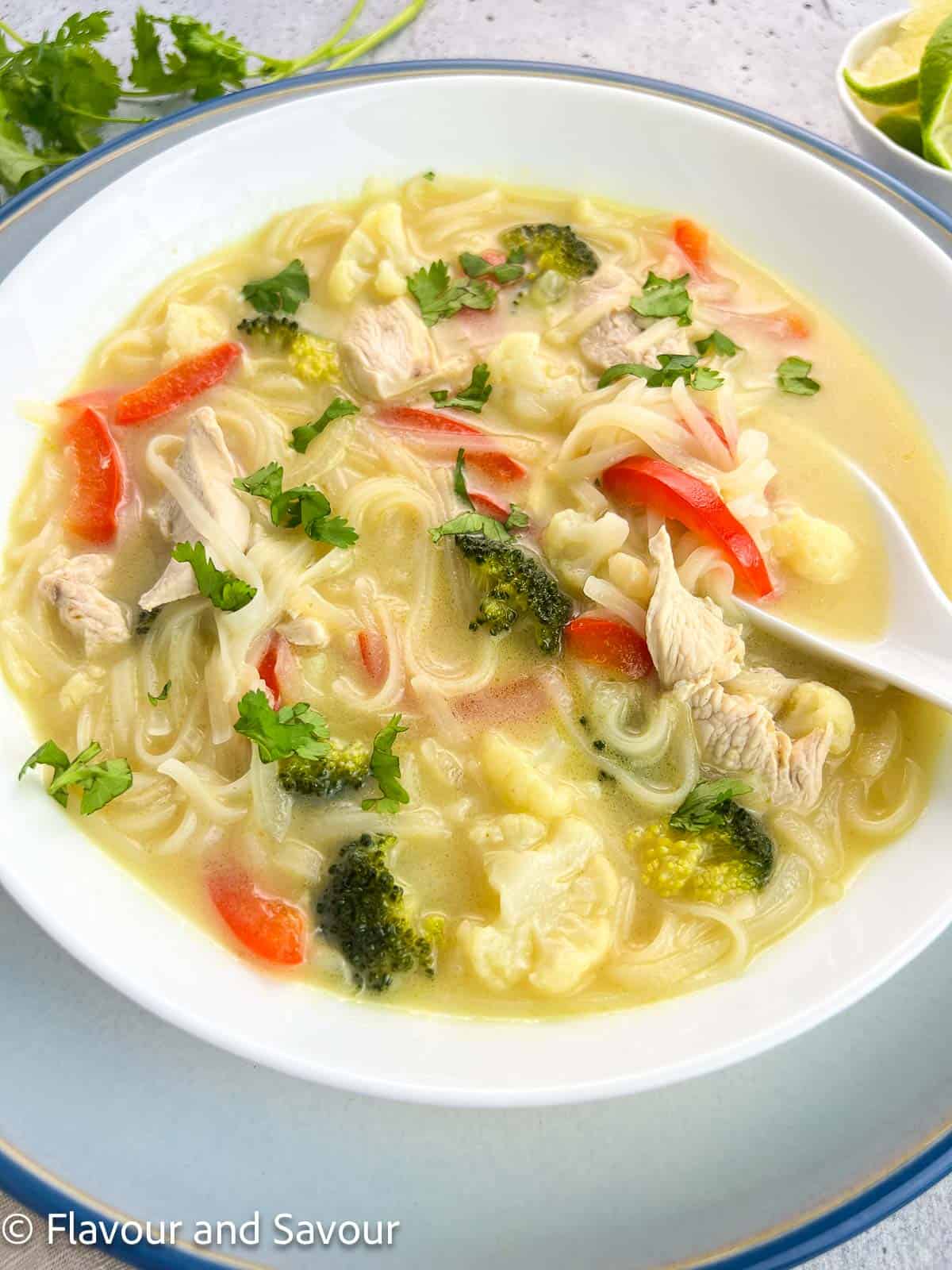 Side view of a white bowl with Thai-inspired chicken soup with rice noodles.
