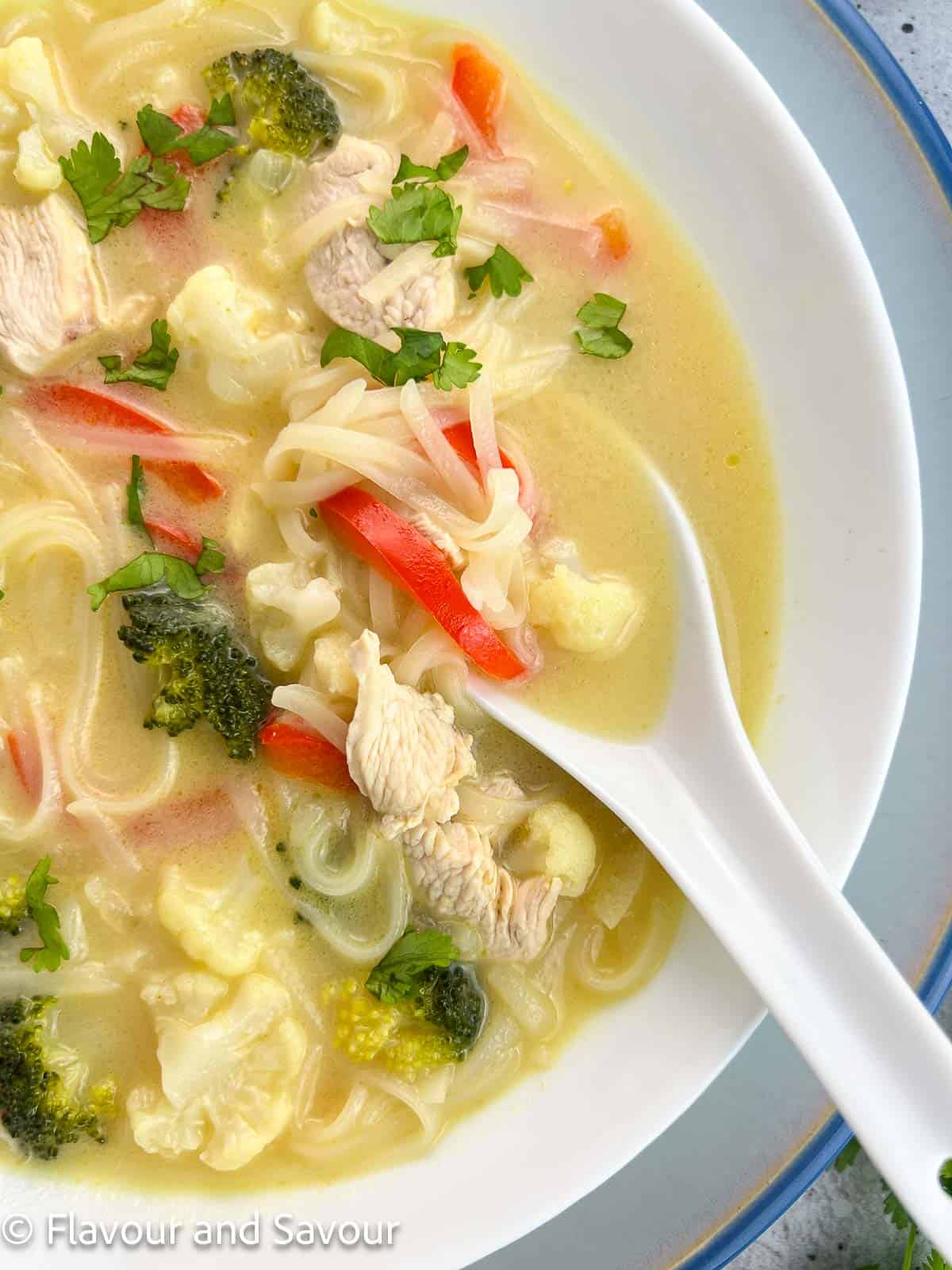 A bowl of Thai green curry chicken soup with a ceramic spoon.