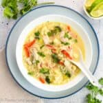 A bowl of Thai chicken noodle soup with a ceramic spoon.