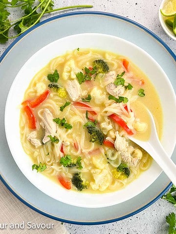 A bowl of Thai chicken noodle soup with a ceramic spoon.