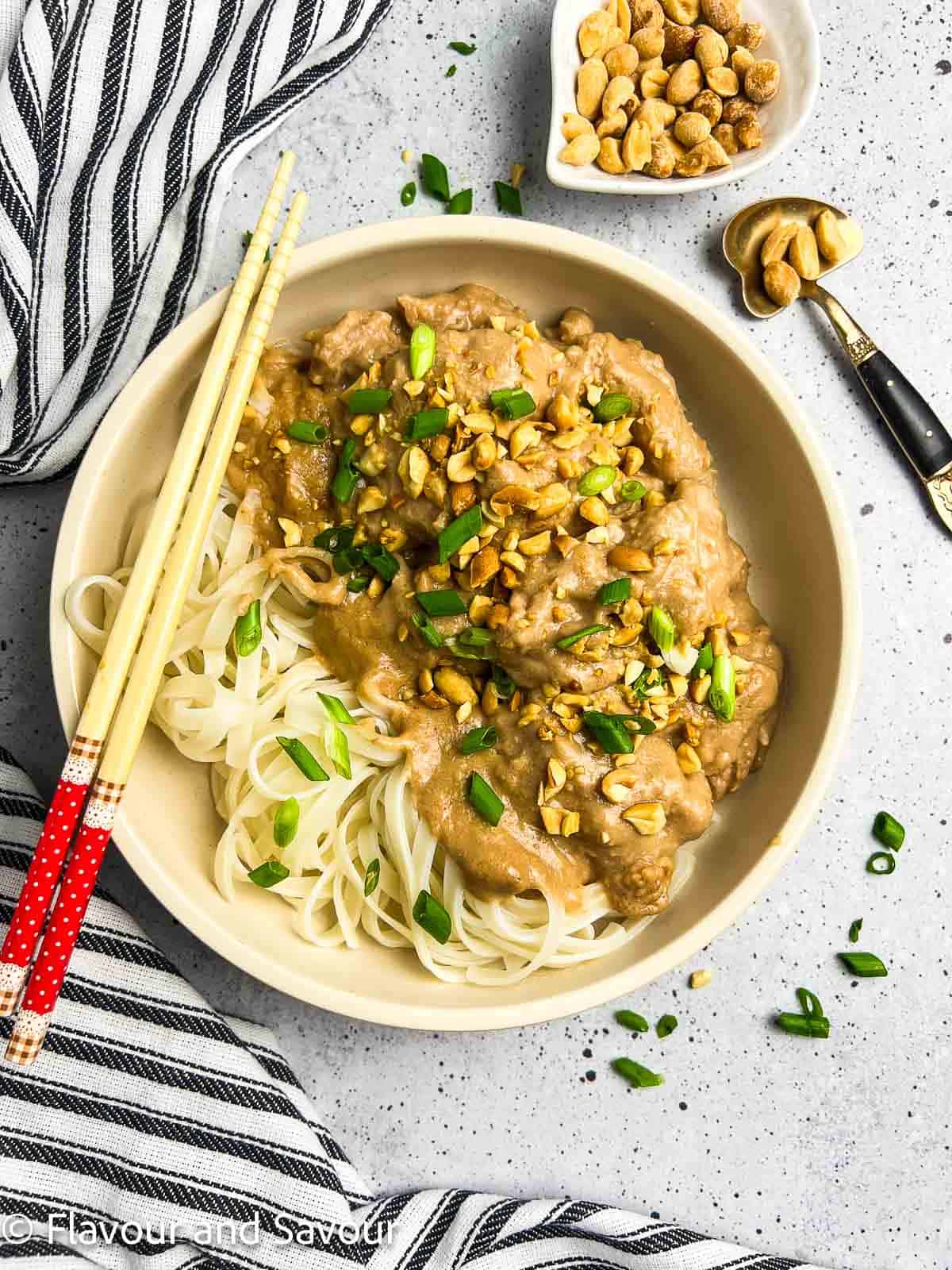 A shallow bowl with Thai peanut chicken and noodles garnished with chopped peanuts and green onions.