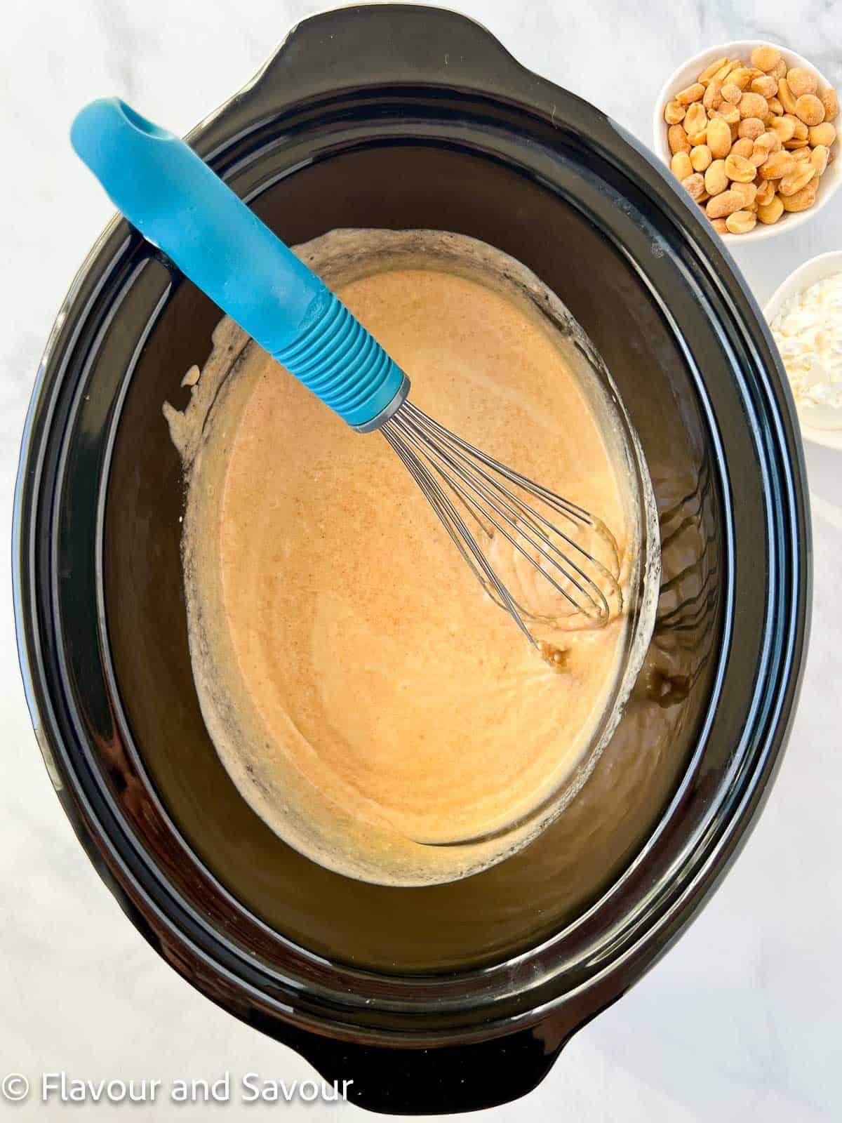 Whisking peanut sauce ingredients together in the bowl of a slow cooker.