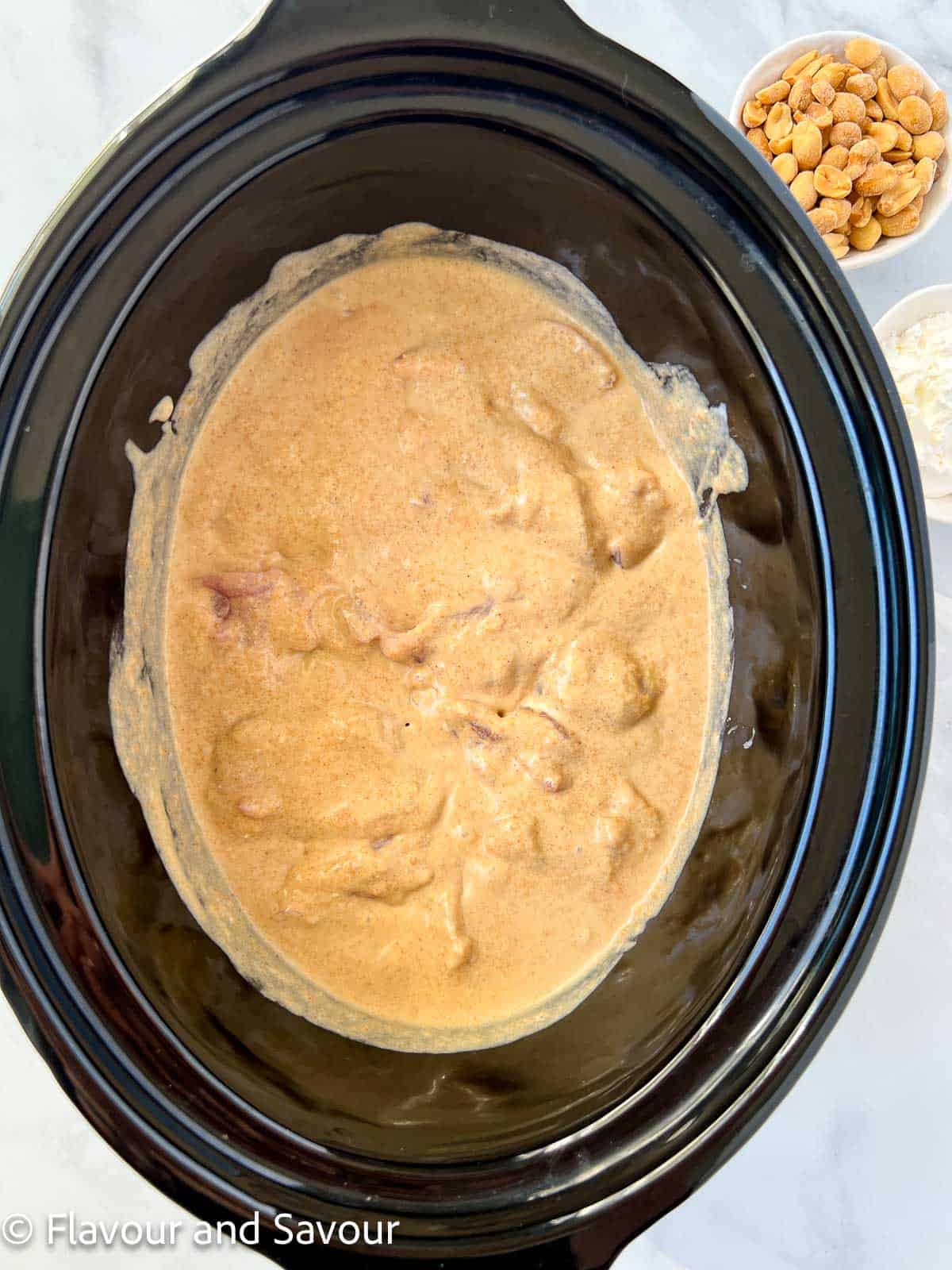 Adding chicken pieces to peanut sauce in the bowl of a slow cooker.