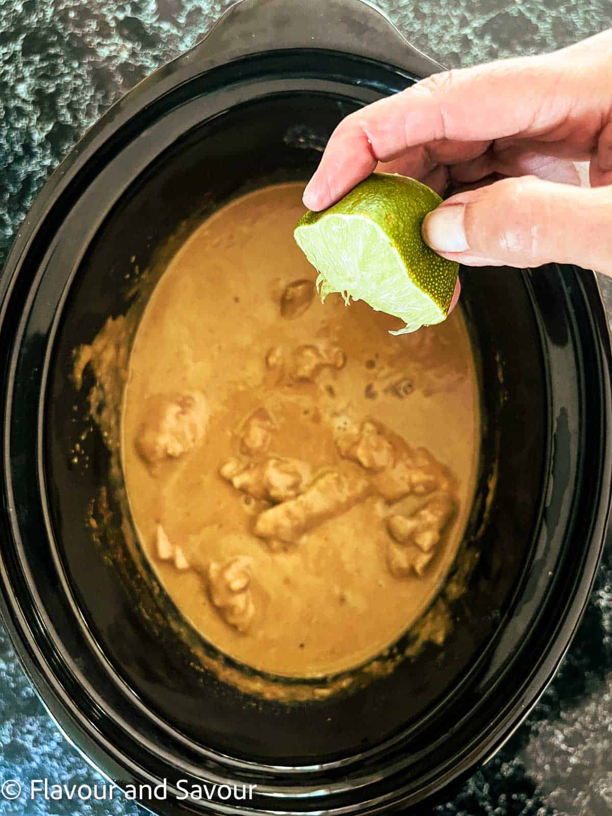 Squeezing lime juice into Thai peanut chicken in a slow cooker.
