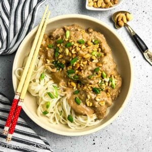 A shallow bowl with Thai peanut chicken and noodles garnished with chopped peanuts and green onions.