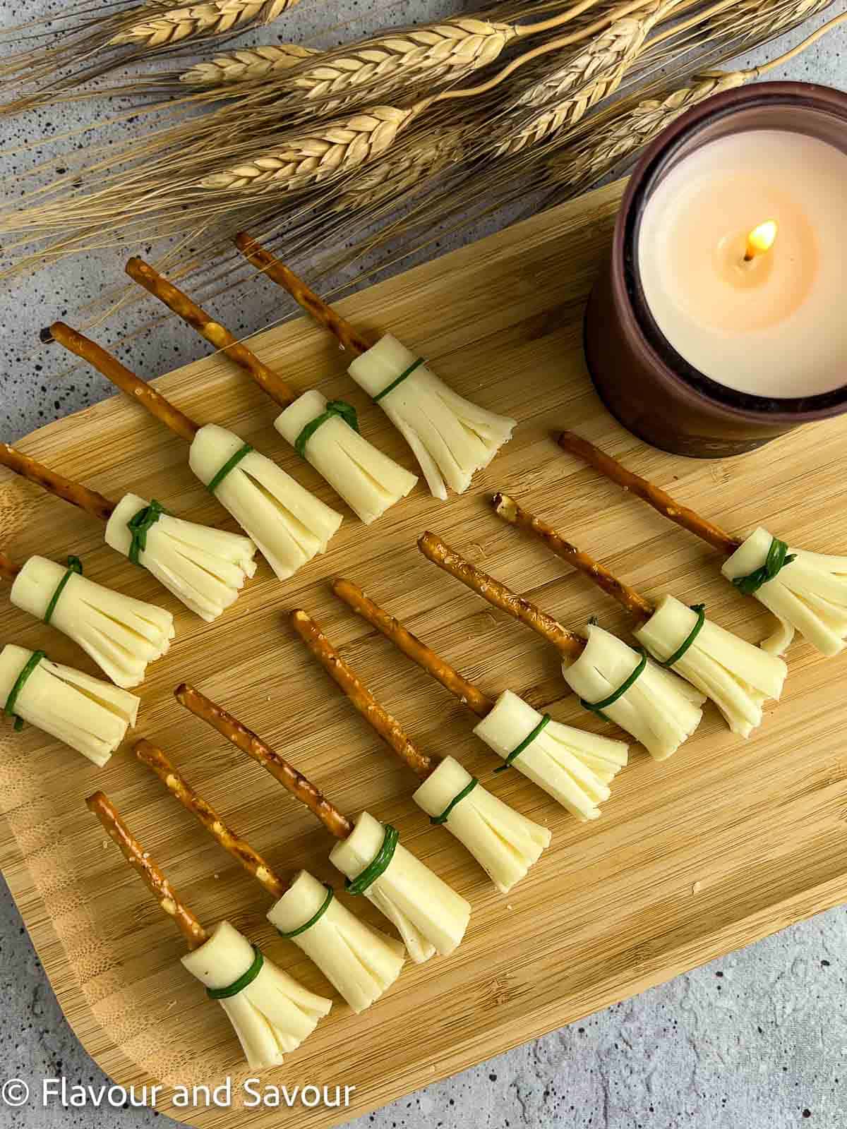 13 cheese and pretzel witches' broomsticks snacks on a serving board.