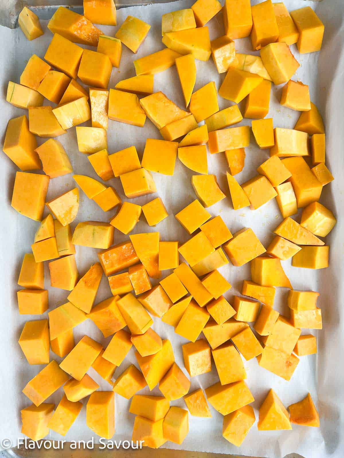 Butternut squash cubes on a parchment-paper lined baking sheet.