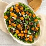 Square image of butternut squash salad in an oval serving bowl.