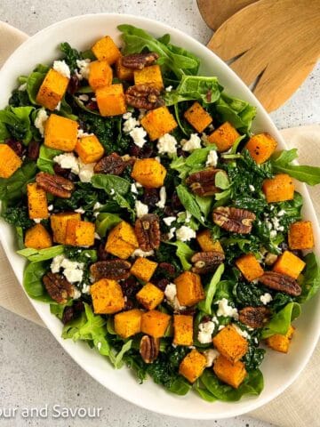 Square image of butternut squash salad in an oval serving bowl.