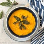 A bowl of butternut squash soup with freshly ground black pepper and toasted sage leaves as garnish.