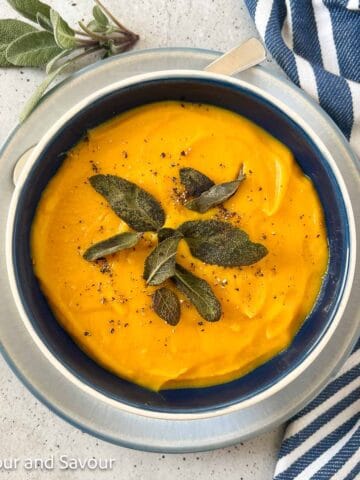 A bowl of butternut squash soup with freshly ground black pepper and toasted sage leaves as garnish.