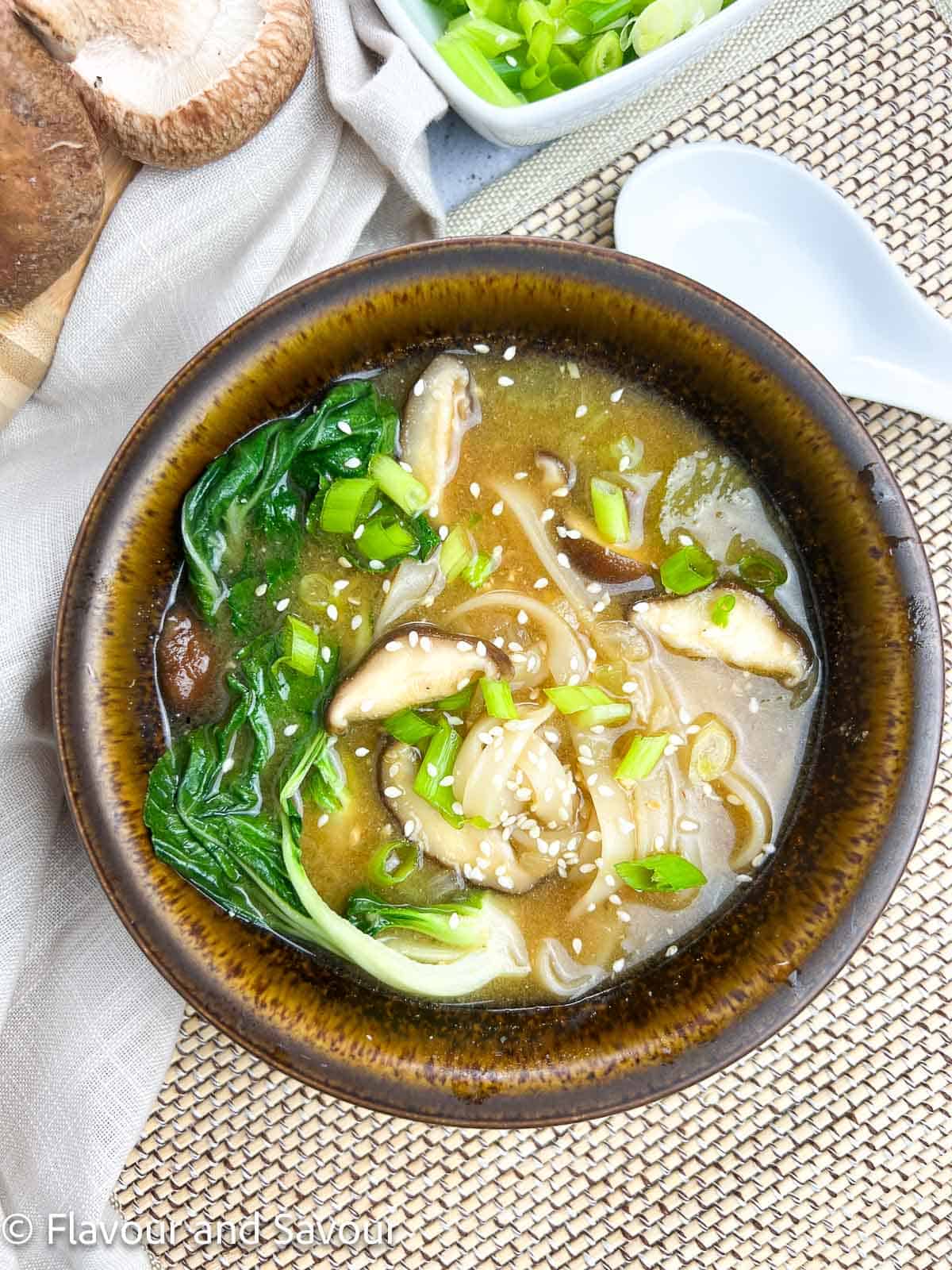 Miso noodle soup with shiitake mushrooms, oyster mushrooms and baby bok choy in a brown stoneware bowl.