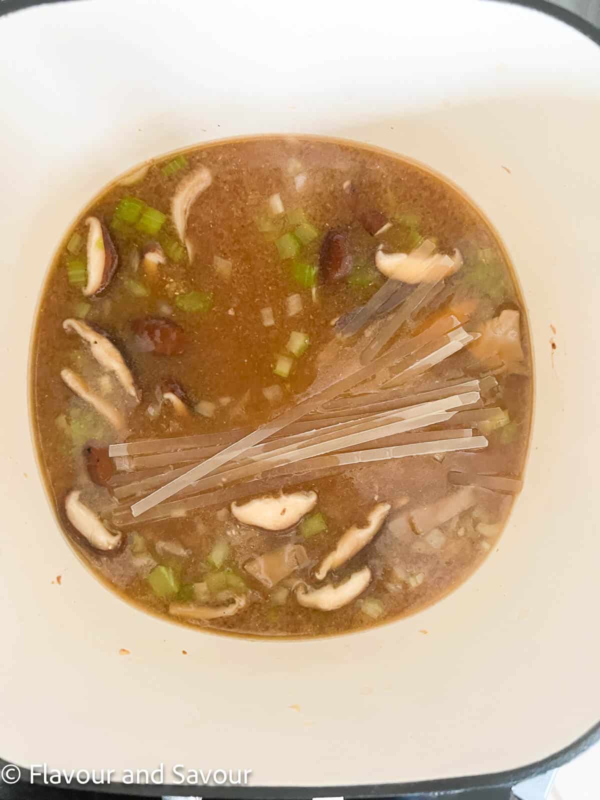 Adding rice noodles to a soup pot to make miso noodle soup.